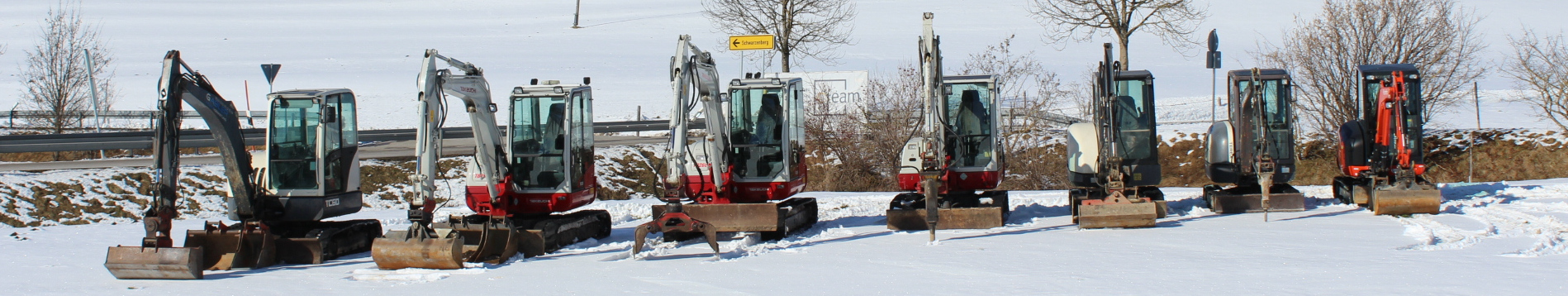 Viele Bagger welche in einer Reihe im Winter stehen.